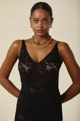 Vestido largo de encaje negro con escote en V y breteles anchos. Presenta un diseño ajustado en el torso que cae con fluidez hacia el ruedo, con una transparencia característica del tejido.