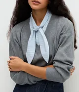 Suéter de punto gris con escote en V y detalle de camisa integrada en color celeste a rayas, con cuello estructurado y lazo frontal. Diseño de corte regular y mangas largas.
