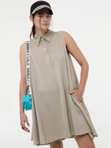 Vestido camisero corto color beige, sin mangas, con cuello clásico, cierre frontal con botones y bolsillos laterales.