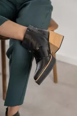 Botineta de cuero negro con diseño combinado en cuero charolado, plataforma y taco cuadrado de madera clara. Presenta cierre lateral y puntera redondeada.