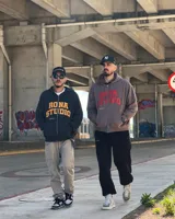 Campera negra con capucha y cierre frontal, con estampado del logo Rona Studio en color naranja en el pecho.