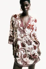 Vestido túnica corto en tejido de viscosa, de corte oversized con hombros caídos y mangas tres cuartos. Presenta escote en V tanto en la parte delantera como en la trasera, con detalles de cenefas estampadas en contraste en el escote, los puños y el ruedo.