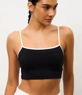 Top deportivo de microfibra con diseño alargado, escote recto y breteles finos. Presenta un detalle de bies contrastante en color blanco en el borde del escote y los breteles. Incluye copas internas para mayor soporte.