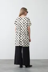 Vestido corto de silueta amplia con corte bajo busto, cuello a la base y mangas cortas. Presenta un estampado de lunares negros sobre fondo beige claro.