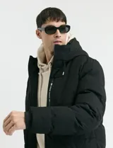 Campera puffer de corte largo, color verde militar, con capucha fija, cierre frontal y puños elásticos internos.