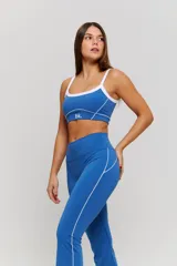 Conjunto deportivo compuesto por un top y un pantalón largo. El top es de estilo deportivo con breteles finos, escote redondo y detalle de ribete blanco en contraste, con el logo 'bk.' estampado en el frente. El pantalón es de tiro alto, ajustado en la cintura y caderas, con diseño acampanado en la parte inferior.