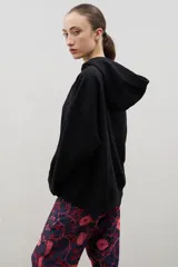 Hoodie negro de corte holgado con capucha y bolsillo tipo canguro frontal. Presenta el logo de la marca bordado en el pecho en color blanco.