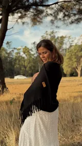 Bufandón de lana merino color negro, de tejido doble y gran gramaje, con terminación de flecos en los extremos y etiqueta de cuero con logo grabado.