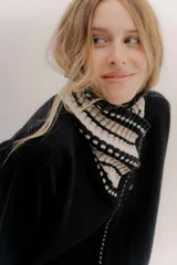 Polera tejida en lambswool color beige, con cuello alto y diseño de intarsia en tonos marrones y grises. Presenta botones forrados en el cuello para modular la apertura.