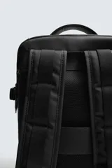 Mochila técnica de color negro con múltiples compartimentos, incluyendo dos bolsillos frontales con cierre, bolsillos laterales y compartimento principal acolchado para dispositivos electrónicos. Cuenta con parte posterior acolchada, banda de sujeción para equipaje, asa de mano y asas de hombro ajustables.