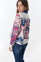 Camisa de lino de manga larga, con cuello y botones frontales. Presenta un estampado artístico y colorido en tonos rosados, azules y blancos, con motivos que recuerdan a escudos o medallones.