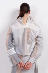 Camisa corta de algodón y seda con silueta recta, diseño a rayas verticales en tonos gris, blanco y beige, cuello camisero, cierre frontal con botones, mangas largas con puños abotonados, bolsillos de parche con botón a presión en el pecho y bajo recto.