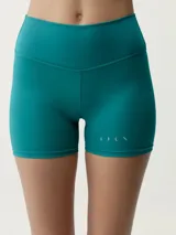 Short deportivo ajustado de tiro alto, color verde azulado, con pequeño logo estampado en la pierna izquierda.