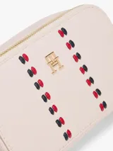 Cartera tipo bandolera de Tommy Hilfiger con acabado granulado, dos compartimentos principales con cierre de cremallera, correa ajustable y monograma TH metálico en la parte frontal junto a una cinta decorativa distintiva.