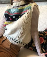 Chaleco de punto artesanal confeccionado en 100% lana merino, con diseño frontal multicolor de patrones geométricos en diagonal sobre base cruda, cuello redondo y terminaciones acanaladas.