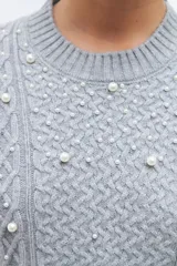 Sweater color beige melange de tejido de punto con diseño de trenzas y detalles de perlas en el frente y las mangas.