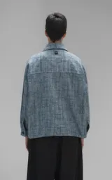 Campera de denim rígido con textura de trama única, corte oversize, cuello camisero, cierre frontal con botones y bolsillos delanteros con solapa.