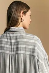 Camisa de manga larga con diseño de rayas verticales en tonos grises y blancos, cuello camisero y cierre frontal con botones.