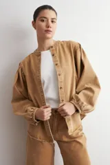 Camisa de jean color camel, de manga larga abullonada, con cuello mao y cierre frontal de botones metálicos.