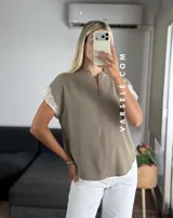 Blusa negra de tela Cey, con cuello mao y escote en V con cierre. Mangas cortas con detalle de encaje marrón en los hombros.