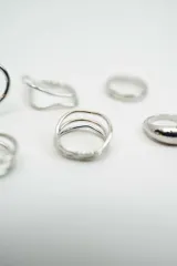 Set de seis anillos de metal plateado con diversos diseños, incluyendo formas geométricas, minimalistas y de estilo alambre.