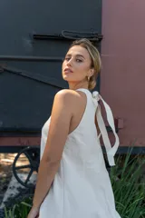 Vestido corto de color beige con cuello halter, diseño sin mangas y cierre frontal con botones dorados.