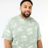 Camiseta de manga corta y cuello redondo en color verde, con estampado integral de palmeras y paisajes tropicales en tono claro.
