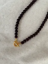 Collar de cuentas esféricas en color marrón oscuro, con cierre frontal tipo marinero en tono dorado.