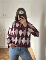 Sweater de punto con diseño de rombos en tonos bordó, gris y rosa, con cuello polo y cierre frontal de botones.