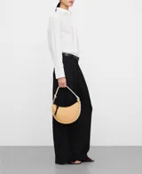 Bolso de hombro tricolor en forma de media luna, confeccionado en material sintético con textura granulada. Cuenta con un compartimento principal con cierre de cremallera, tirador con nudo negro, bolsillo interior con cremallera, asa corta tubular en tono claro con detalle metálico y logo grabado en la parte frontal.