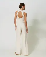 Mono largo color crema de lino y viscosa, con cuello halter, cintura entallada, pantalón ancho con abertura frontal profunda y cierre lateral.
