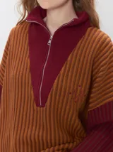 Pullover de tejido acanalado grueso con diseño bicolor en tonos marrón y bordó. Presenta cuello alto con cierre frontal, mangas largas y corte holgado.