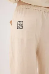 Pantalón de lino color beige, de silueta relajada, tiro medio-alto, cintura elastizada con cordón ajustable, bolsillos laterales y bolsillos traseros.