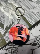 Llavero redondo con ilustración de dos personajes masculinos de anime, con aro metálico y cadena.