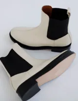 Bota Chelsea color hueso de cuero vacuno, con elástico lateral negro y suela de cuero.