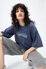 Remera azul de manga corta con estampa de caballo y texto "It's about to get WESTERN".