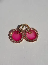 Aros tipo argolla dorados con dije redondo de resina fucsia, rodeado de strass.