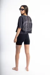 Remera de corte boxy fit, color negro con efecto lavado, de manga corta y cuello redondo. Presenta un logo bordado en el centro del pecho dentro de un óvalo.