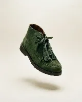 Bota de caña media confeccionada en cuero gamuzado color marrón chocolate. Presenta un diseño de estilo mocasín con cordones frontales decorados con borlas desmontables y suela plana de goma resistente.