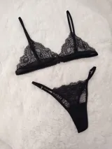 Conjunto de lencería de encaje negro, compuesto por un soutiene tipo triángulo con tirantes finos regulables y una bombacha cavada con tiras laterales regulables.