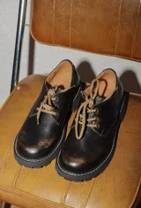 Borcego de cuero en tono marrón oscuro con efecto desgastado, cordones bicolor y suela track dentada de goma negra.