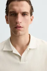 Polo de manga corta color verde oliva, con cuello solapa y abertura frontal tipo polo. Presenta una textura acanalada vertical y un calce regular.