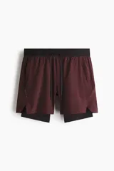 Short deportivo de doble capa en tejido funcional con tecnología DryMove para absorción de sudor. Presenta corte estándar, cintura elástica con cordón ajustable, bolsillos laterales y aberturas en el bajo. Incluye una capa interior tipo biker con bolsillo y bucle trasero para accesorios.