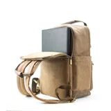 Mochila urbana de tela canvas color marrón, con diseño funcional que incluye compartimento para notebook de 15 pulgadas y espacio interior organizado para set de mate. Cuenta con correas ajustables, manija superior reforzada, bolsillo frontal con cierre y detalles en cuero sintético.