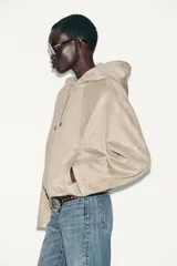 Chaqueta bomber de efecto ante en color marrón, con capucha ajustable mediante cordones, cierre frontal con cremallera, bolsillos laterales y bajo con elástico interior.