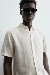 Camisa de lino color beige de corte relajado, con cuello solapa, manga corta y cierre frontal con botones.