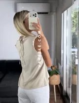 Blusa blanca sin mangas, de símil lino, con cuello alto y detalle de encaje calado y volados en el escote.