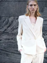 Chaqueta de corte recto y diseño minimalista en color crema, con cuello de solapa, cierre frontal de doble botonadura y forro interior.
