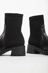 Bota de caña media color negro, con diseño tipo chelsea, suela track con detalle de tachas metálicas en el borde y elástico lateral.