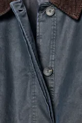 Chaqueta encerada de corte recto con cuello de solapa en pana marrón. Presenta manga larga, bolsillos delanteros de vivo y de plastrón con solapa, y un cinturón de lazada en el mismo tejido. Incluye cierre frontal con botones ocultos por tapeta y abertura en la espalda.